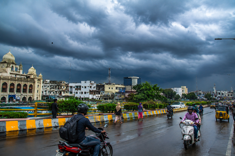 Telangana Monsoon 2026: Rainy Season Likely to Arrive by June 11 1 Commuters travel through a Hyderabad city roadway under dense monsoon clouds as rain-bearing weather systems approach Telangana during the monsoon season.